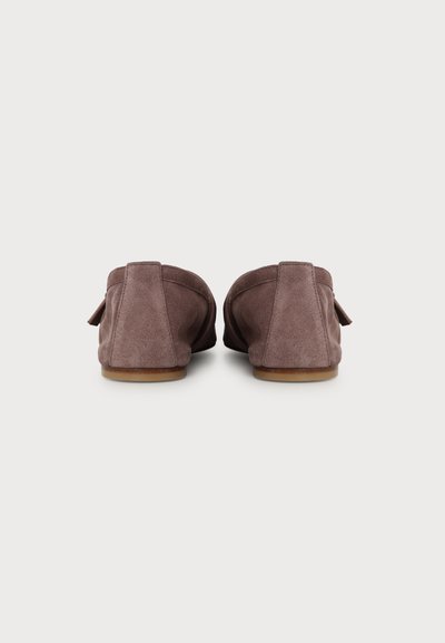 Paire de mocassins en daim marron vues de dos, semelles plates en bois, texture de tissu douce, fond neutre.