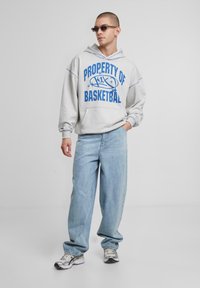 Szürke kapucnis pulóver, amelyen kék színű felirat olvasható: "BASKETBALL TULAJDONA", világoskék farmernadrággal és fémes sportcipővel párosítva. Sima szövettextúra.
