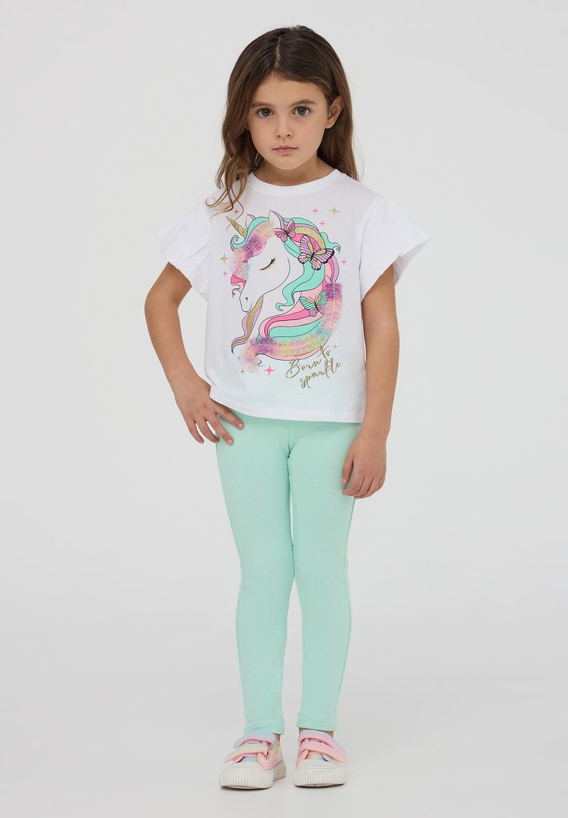 T-shirt bianco con una grafica di unicorno nei colori pastello, abbinata a leggings verde menta e sneakers rosa chiaro con fiocchi.