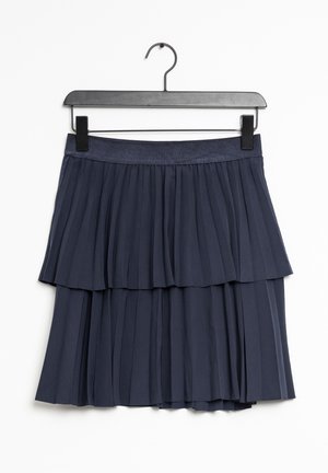 Gonna a pieghe a balze di colore blu navy con una vita testurizzata, appesa a un gancio nero su uno sfondo bianco.