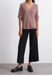 Pullover rosa a V with costine abbinato a pantaloni neri a gamba larga. Mocassini neri completano l'outfit. Maglione lavorato e vestibilità rilassata.