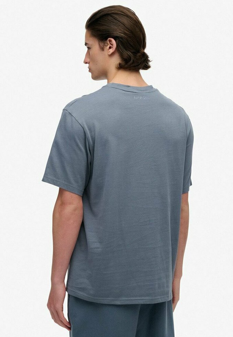 Camiseta de algodón gris con mangas cortas y cuello redondo. Presenta un logo sutil en la parte posterior. Textura suave y ajuste relajado.