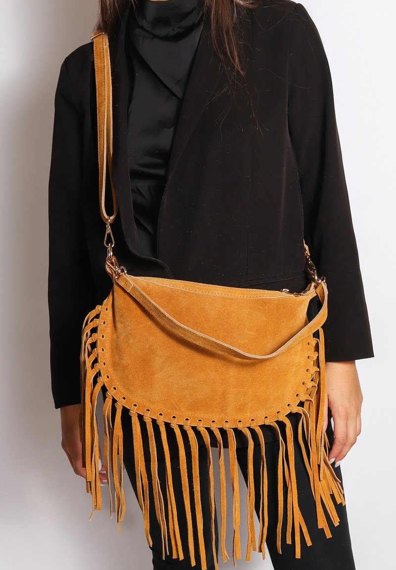 Cognac suède schoudertas met franjes langs de onderrand, ronde vorm en een enkele schouderriem met hardware-accenten.