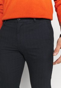 Tmavě modré, texturované kalhoty s rovnými nohavicemi, se zapínáním na přední knoflík a bočními kapsami, doplněné červeným svetr.