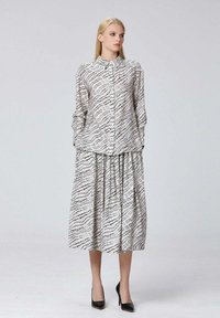 Robe chemise à manches longues en tissu doux, avec un motif en damier noir sur fond blanc, dotée d'une fermeture à boutons et d'une jupe plissée.