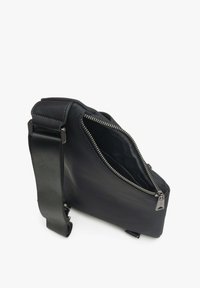 Czarna skórzana torba na ramię o teksturowanym wykończeniu, z ukośnym zamkiem błyskawicznym, regulowanym paskiem i subtelnymi metalowymi dodatkami.