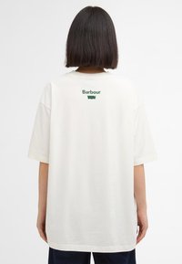 Valge ülev suurusega T-särk lühikeste varrukatega, mille ülemisel seljal on roheline "Barbour" logo. Sile tekstuur ja juhuslik istuvus.