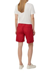 Rode katoenen shorts met een elastische tailleband en omgeslagen zoom. Gecombineerd met een witte shirt met korte mouwen en lichte sneakers.