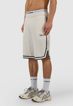 Male wearing white basketball shorts with black trim, white branded socks, and beige running shoes, standing against plain background.