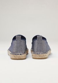 Espadrilles en tissu tissé bleu marine et crème avec semelle en corde de jute, vue arrière ; comportent une languette de talon en boucle et un motif à carreaux sur les côtés.
