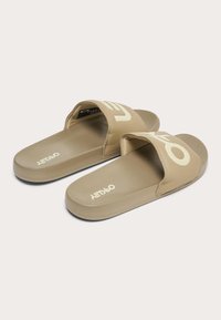 Coppia di sandali beige aperti con suola imbottita e ampie fasce con scritte audaci di colore chiaro.