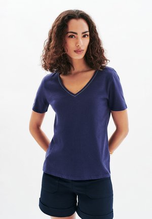 T-shirt bleu marine à manches courtes et en V, avec une texture douce et des détails de couture légers le long du col. Associé à un short foncé.