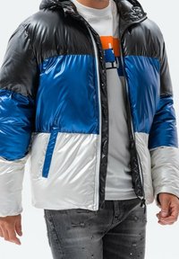 Farbenfrohe Steppjacke in Schwarz, Blau und Silber mit glänzendem Material, Reißverschluss und Seitentaschen.