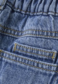 Denimtyg i ljusblått med framträdande gult stygn. Har en insamlad midjeband och en liten framficka.