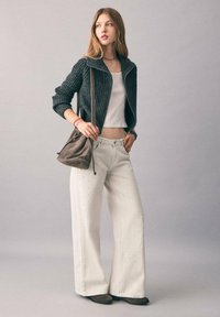 Chaqueta gris de cremallera con canalé, top corto blanco, pantalones anchos blancos con perforaciones, bolso cruzado marrón y zapatos planos marrones. Paleta de colores neutros.