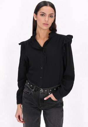 Camicia nera con bottoni, caratterizzata da un colletto e polsini con volant, abbinata a jeans grigio scuro a vita alta e una cintura nera con dettagli in metallo.