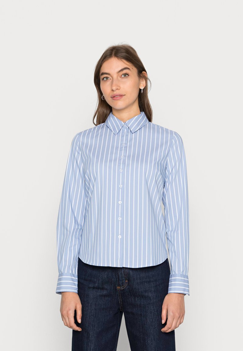 Camicia azzurra chiara con righe bianche verticali, maniche lunghe, colletto appuntito e orlo arrotondato. Vestibilità casual, tessuto morbido.