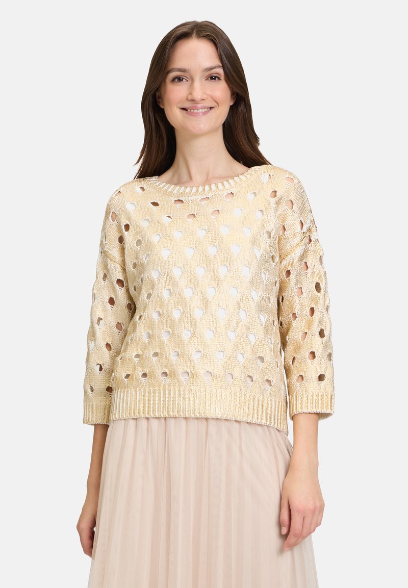 Goldfarbener gestrickter Pullover mit lockerer Passform, der offene Webmuster, Dreiviertelärmel und einen gerippten Saum aufweist. Glatte Textur.