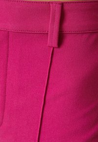 Fuksjowe spodnie o gładkiej fakturze, z płaskim paskiem w talii, delikatnym przeszyciem i bez widocznych elementów metalowych.