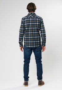 Flanellen overhemd in een donkergroen, marineblauw en wit geruit patroon. Heeft lange mouwen en een rechte zoom. Gecombineerd met donkerblauwe jeans en bruine laarzen.