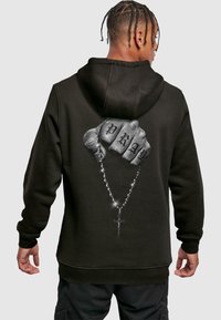 Felpa nera con cappuccio caratterizzata da una grafica di un pugno chiuso con "PRAY" tatuato sulle nocche, che tiene un rosario con un dettaglio a forma di croce.