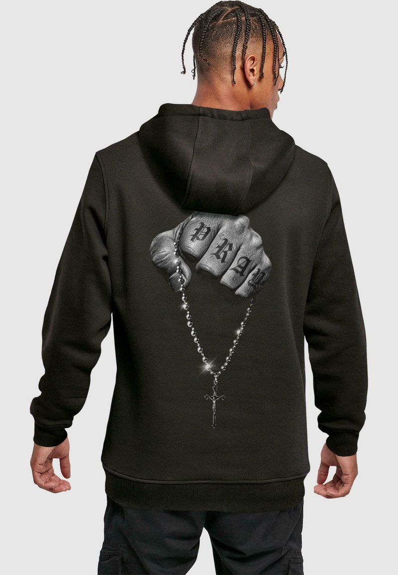 Felpa nera con cappuccio caratterizzata da una grafica di un pugno chiuso con "PRAY" tatuato sulle nocche, che tiene un rosario con un dettaglio a forma di croce.