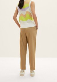 Bezrękawnik dzianinowy w falisty wzór w kolorach zielonym, lawendowym i beżowym; połączony z jasnobeżowymi spodniami i białymi trampkami z beżowymi akcentami.