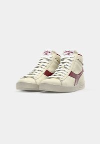 High-top sneakers made of cream leather with a maroon accent, white laces, and textured rubber sole. Logo on tongue and side.