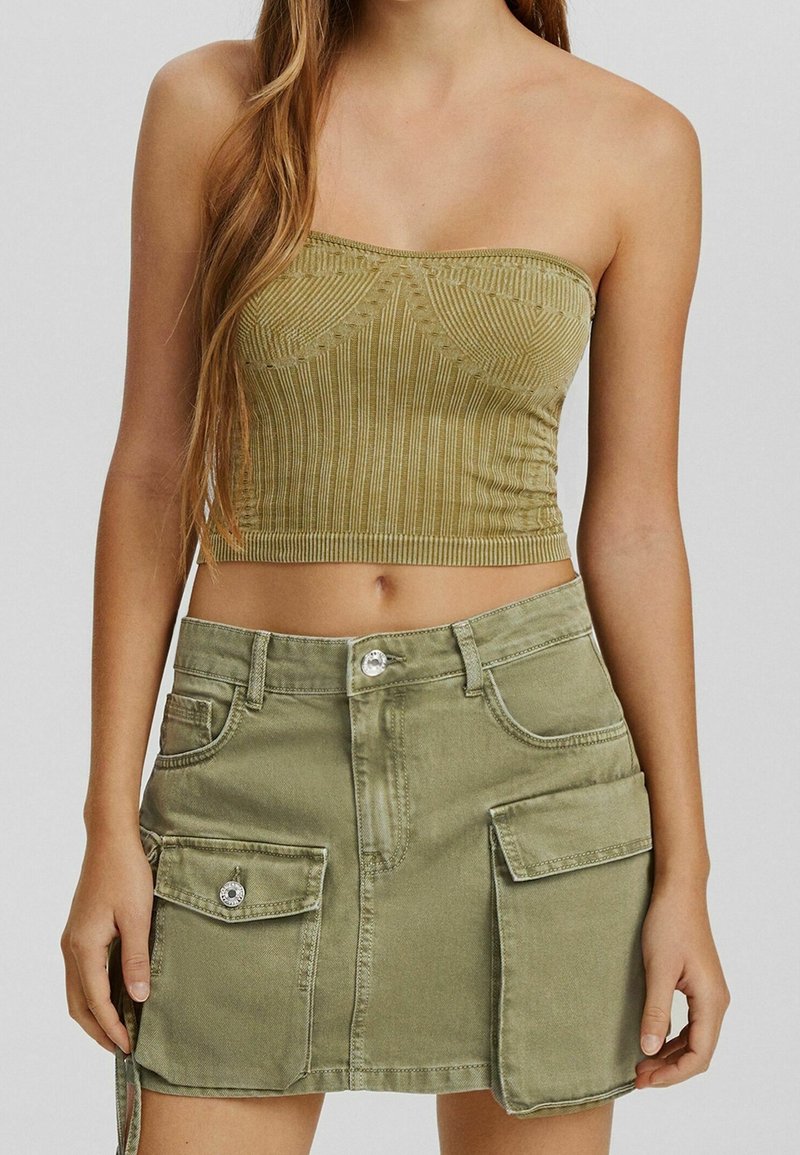 Top corto sin mangas de color verde oliva con detalles de costura, combinado con una falda de mezclilla verde oliva a juego que cuenta con bolsillos frontales y cierre de botones.