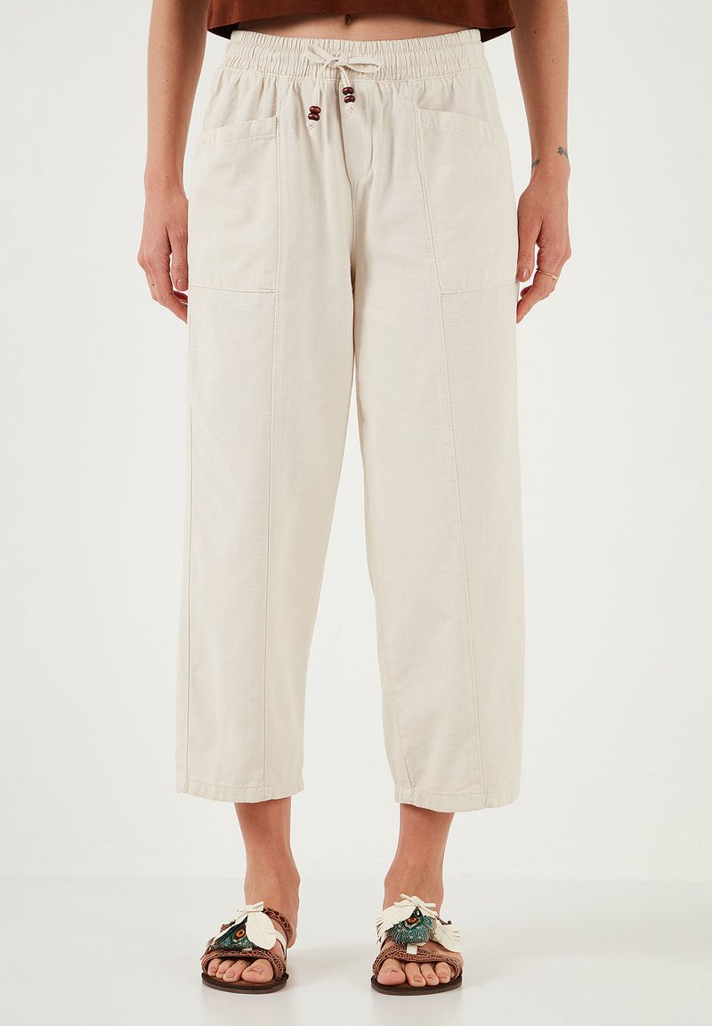 Beige, lightweight, wide-leg trousers with an elastic waistband, drawstring, and two front pockets. Textured fabric with a relaxed fit.