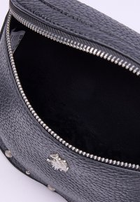 Černá texturovaná kožená taška se zipovým uzávěrem, zobrazující vnitřní podšívku. Disponuje stříbrnými kovanými prvky a dekorativními emblémy na boku.