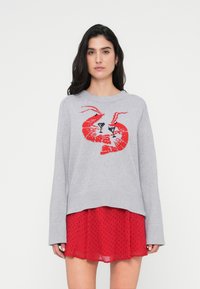 Pull gris en tricot avec un motif homard rouge et des verres à cocktail. Superposé sur une jupe rouge à pois. Manches longues et coupe décontractée.