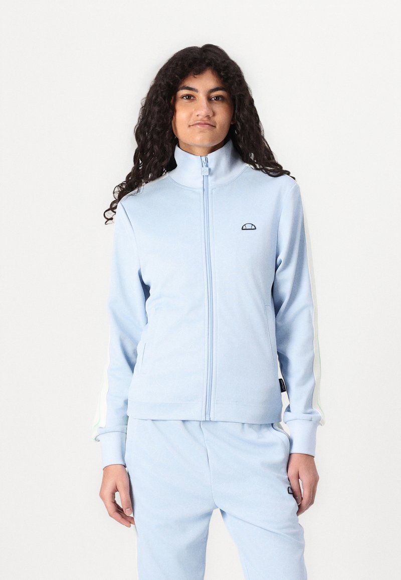 Lys blå zip-up hettegenser laget av myk stoff, med stående krage, subtilt logo og hvit-grønt stripete detaljer på ermene.