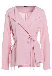 Blouse portefeuille rose pâle à manches longues avec larges revers et cordons de taille noués sur un fond uni.