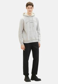 Sudadera gris con un bolsillo frontal y cordones, con texto en negro. Combinada con pantalones negros y botas negras con cordones.