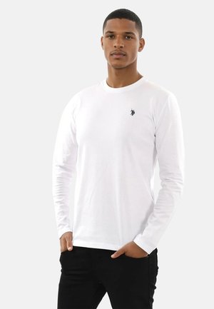 Langarm-weißes T-Shirt aus Baumwolle, mit kleinem schwarzem Logo auf der Brust, kombiniert mit schwarzen Hosen. Einfaches Design, glatte Textur.