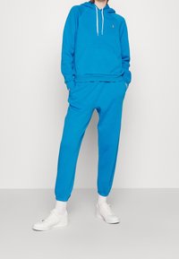 Blå bomullshoodie med en känguruficka och vita dragsnören, kombinerad med matchande joggerbyxor med elastiska avslut och en avslappnad passform.