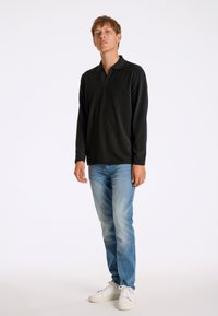 Svart långärmad polo med ribbad textur, krage, matchad med ljusblå raka jeans och vita sneakers.