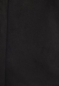 Primo piano di un tessuto scamosciato nero con texture visibile e una cucitura sul lato sinistro.