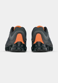 Mustad spordijalatsid oranžide detailidega, iseloomulik sujuv disain, tekstureeritud pealmine osa ja jäme, läikiv tallaosa nähtava soonte mustriga.