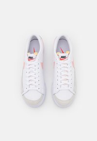 Zapatillas Nike con una parte superior de cuero blanco predominante, acentos en rosa, paneles de gamuza gris texturizada y un diseño clásico de cordones.