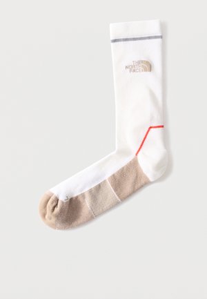 Witte enkelsok met beige teen en zool, grijze streep bij de boord, rood accent vlakbij de hiel, en het "The North Face" logo op de kuit.