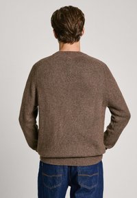 Suéter de punto marrón con cuello redondo y puños y dobladillo acanalados. Presenta un tejido texturizado y un corte relajado, mostrado desde la parte posterior.
