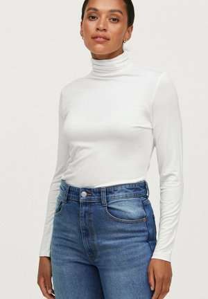 Weißes langärmliges Turtleneck-Shirt aus glattem Material, kombiniert mit hochtaillierten blauen Jeans aus Denim mit Knopfverschluss und Vordertaschen.