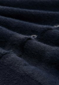 Marineblaues Fleece-Gewebe mit weicher Textur, sichtbaren Nähten und schwarzen Knöpfen. Detaillierte Nahaufnahme von Falten und Oberfläche.