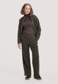 Fleece-Jacke in Dunkelgrün mit hohem Kragen, kombiniert mit passenden weit geschnittenen Hosen. Der Stoff hat eine weiche Textur und ist für höchsten Komfort designed.