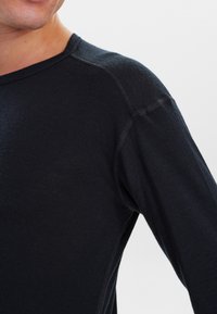 Dark long-sleeve shirt with a crew neck. Made of smooth fabric, features contrast stitching on shoulders, and a fitted silhouette.