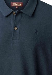 Polo bleu marine texturé avec deux boutons, un col et un petit logo sombre brodé sur le côté gauche de la poitrine.
