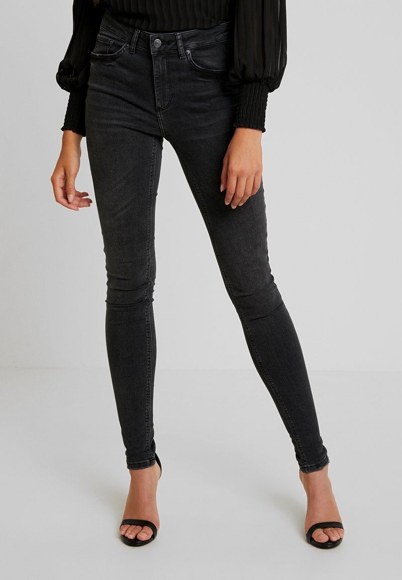 Jeans negros ajustados de talle medio, con un diseño de cinco bolsillos, con un desgaste mínimo y una textura suave, combinados con tacones negros.