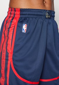 Marineblå basketballshorts med røde side-striber, meshtekstur, elastisk talje, NBA-logo og detalje med teksten "Golden State Warriors".